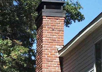 Square red brick chimney with black flue cover