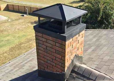 Square red brick chimney with black flue cover - nice field in the background